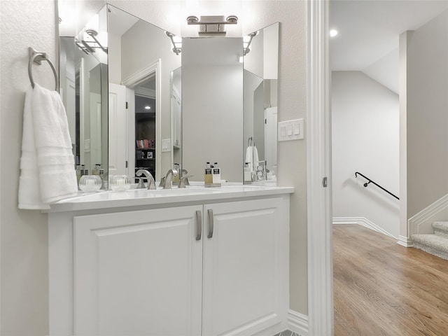 bathroom with vaulted ceiling, vanity, baseboards, and wood finished floors