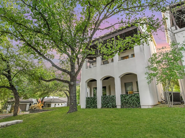 exterior space featuring a yard, a balcony, central AC unit, and stucco siding