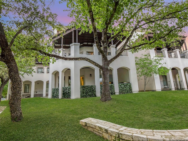 exterior space with stucco siding, a lawn, and a balcony