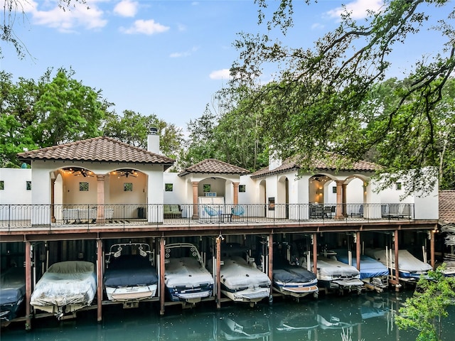 rear view of house featuring covered parking, a tile roof, stucco siding, a chimney, and boat lift