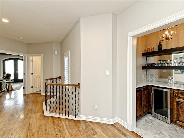 bar with light wood-style flooring, bar, wine cooler, arched walkways, and baseboards