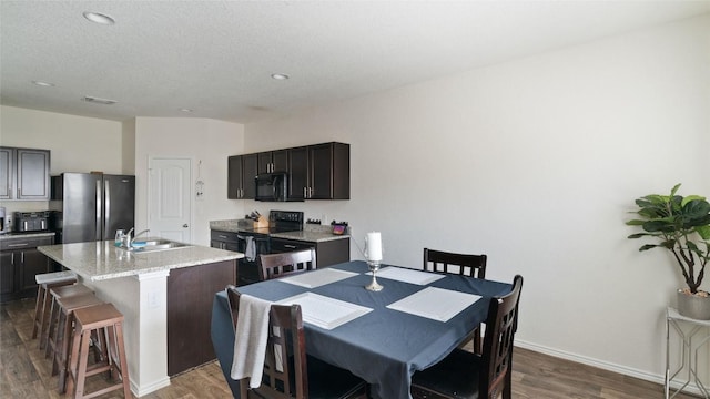 kitchen featuring dark wood-type flooring, a breakfast bar, sink, a center island with sink, and black appliances