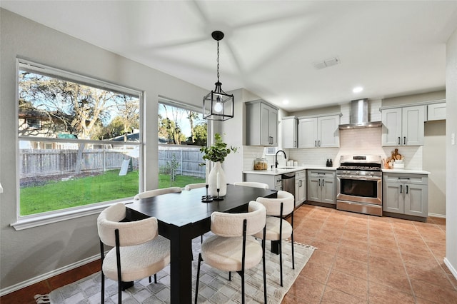 kitchen featuring wall chimney exhaust hood, appliances with stainless steel finishes, gray cabinets, and pendant lighting