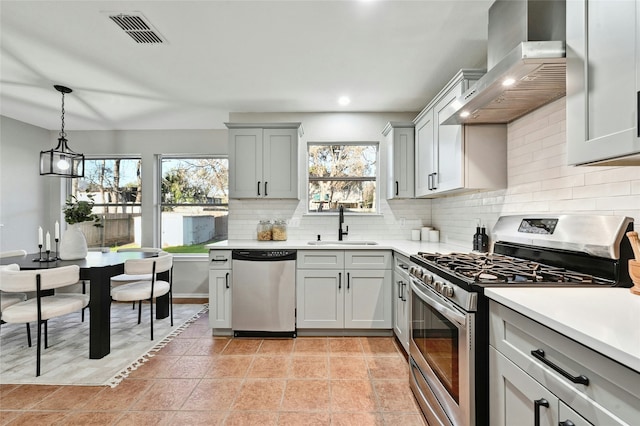 kitchen featuring wall chimney range hood, stainless steel appliances, sink, backsplash, and light tile patterned floors