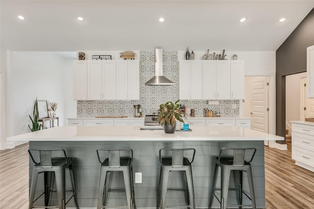 kitchen with wall chimney exhaust hood, white cabinets, a kitchen breakfast bar, and a spacious island