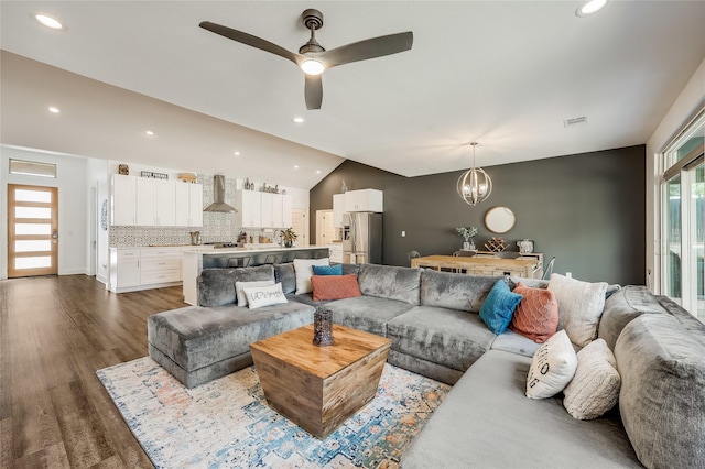 living room featuring ceiling fan with notable chandelier, vaulted ceiling, and dark hardwood / wood-style flooring