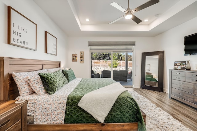 bedroom with access to exterior, ceiling fan, wood-type flooring, and a tray ceiling