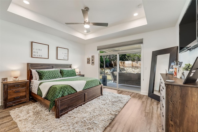 bedroom with access to outside, light hardwood / wood-style flooring, a raised ceiling, and ceiling fan