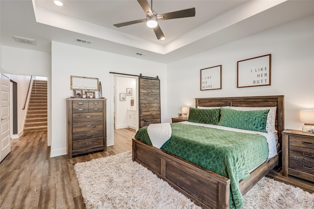 bedroom with ceiling fan, wood-type flooring, a raised ceiling, and a barn door