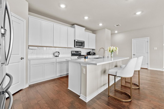 kitchen with white cabinets, appliances with stainless steel finishes, tasteful backsplash, an island with sink, and sink