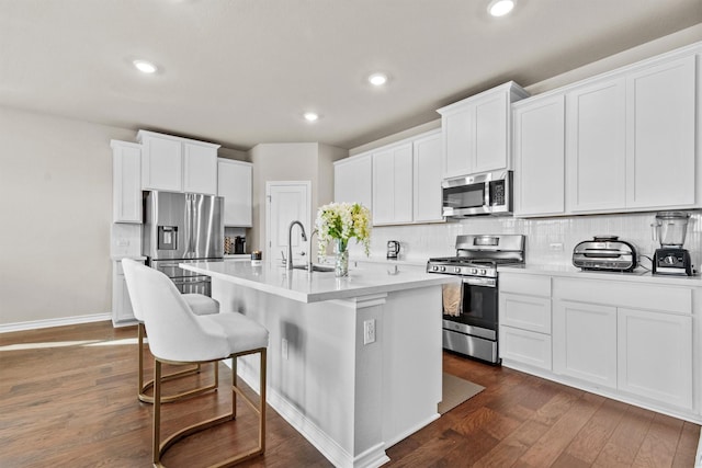 kitchen with dark hardwood / wood-style flooring, appliances with stainless steel finishes, white cabinets, tasteful backsplash, and an island with sink