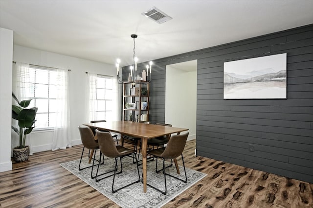 dining room with wood-type flooring, wood walls, and an inviting chandelier