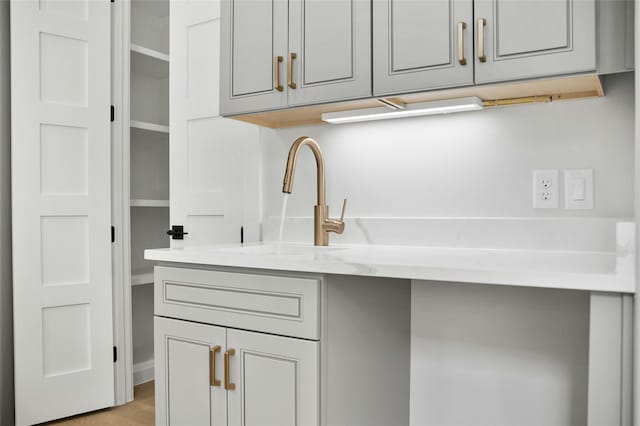 kitchen featuring sink, light wood-type flooring, light stone counters, and gray cabinets