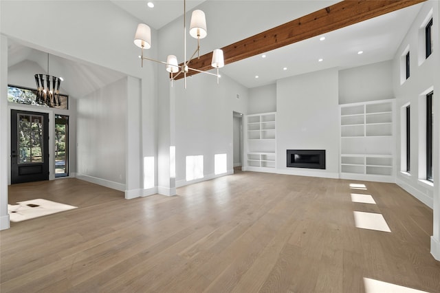 unfurnished living room with built in features, light wood-type flooring, a high ceiling, and a notable chandelier