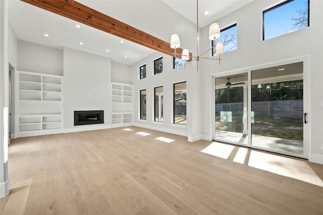 unfurnished living room featuring built in shelves, a healthy amount of sunlight, and a towering ceiling