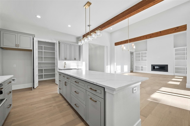 kitchen with pendant lighting, a center island, beamed ceiling, light stone counters, and gray cabinetry