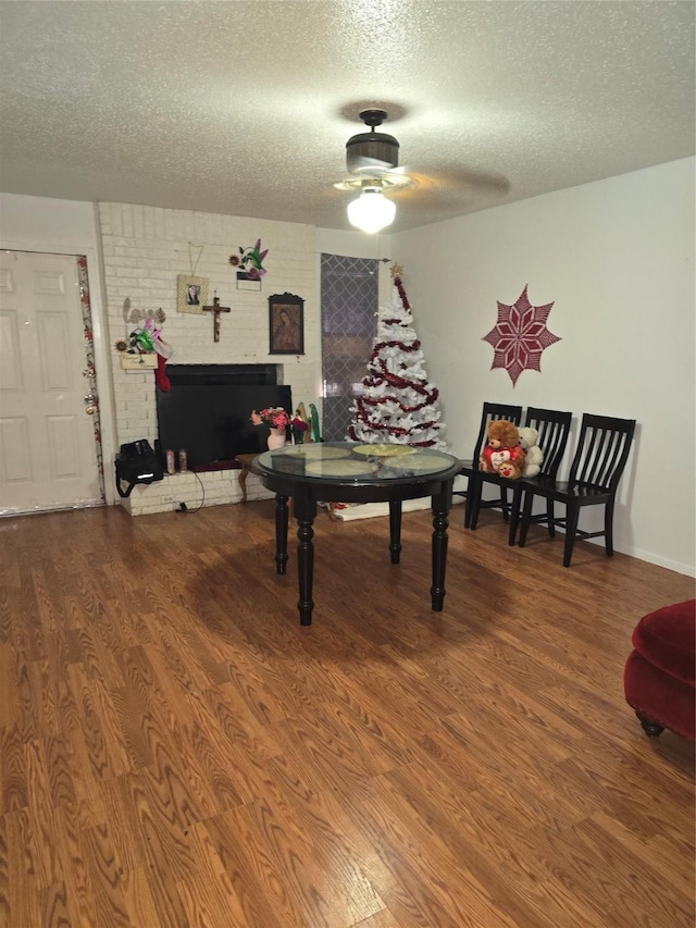 game room with ceiling fan, a fireplace, a textured ceiling, and wood-type flooring