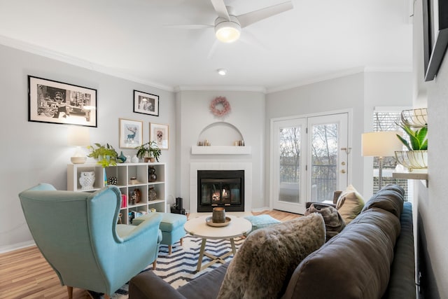 living room featuring ceiling fan, hardwood / wood-style floors, a tile fireplace, and ornamental molding