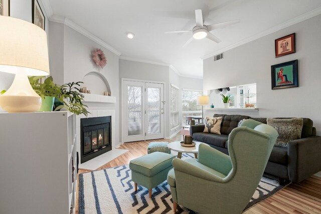 living room featuring light hardwood / wood-style floors, a tile fireplace, crown molding, and ceiling fan