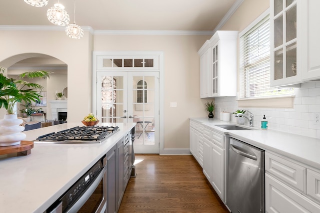 kitchen with appliances with stainless steel finishes, white cabinetry, hanging light fixtures, sink, and ornamental molding