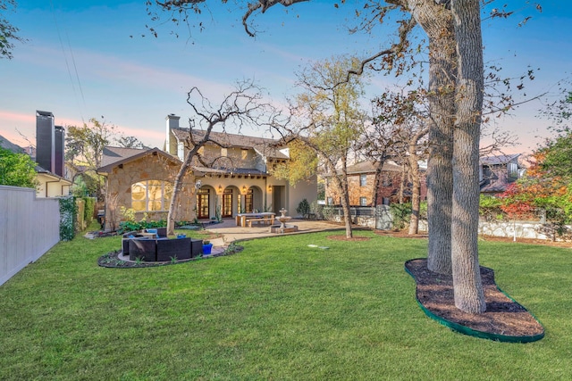 back house at dusk featuring a patio and a lawn