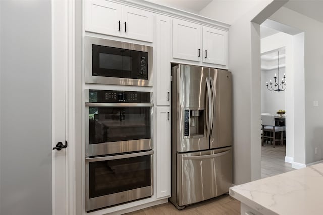 kitchen featuring light hardwood / wood-style flooring, appliances with stainless steel finishes, white cabinetry, light stone counters, and an inviting chandelier