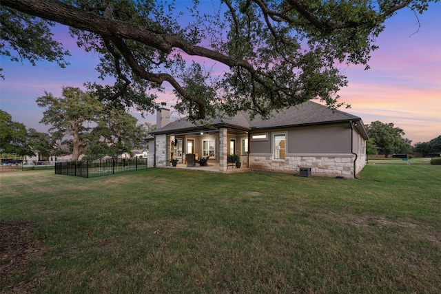 back house at dusk featuring a yard and a patio