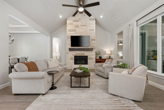 living room featuring a stone fireplace, hardwood / wood-style floors, vaulted ceiling, and ceiling fan