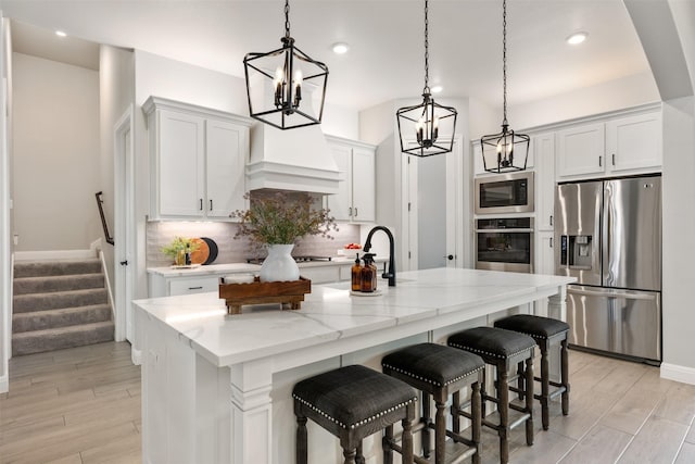 kitchen with light stone countertops, white cabinets, decorative light fixtures, stainless steel appliances, and a kitchen island with sink