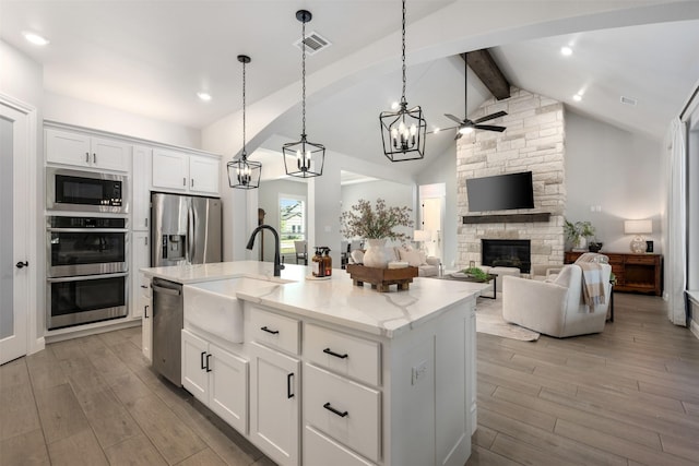 kitchen with decorative light fixtures, white cabinetry, stainless steel appliances, sink, and a kitchen island with sink