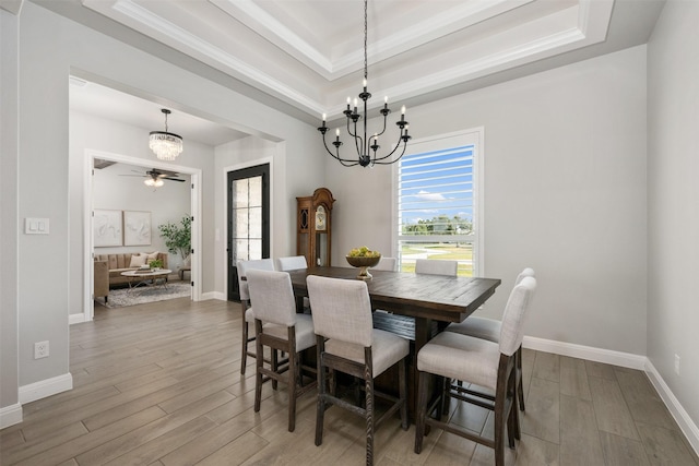 dining area with ornamental molding, ceiling fan with notable chandelier, hardwood / wood-style floors, and a tray ceiling