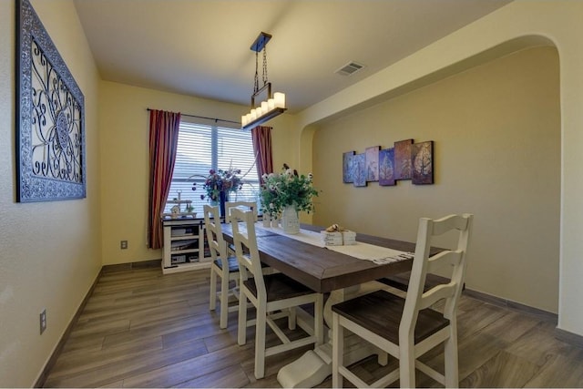 dining room featuring arched walkways, visible vents, baseboards, and wood finished floors