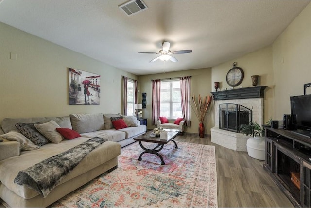 living area with ceiling fan, a fireplace, wood finished floors, and visible vents