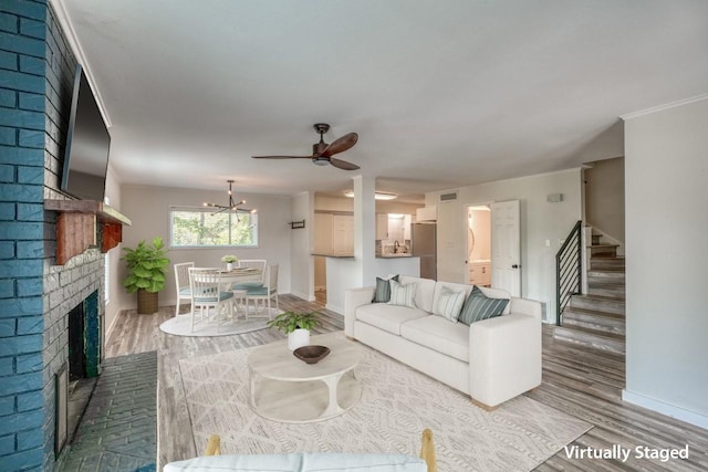 living room featuring hardwood / wood-style flooring, ceiling fan with notable chandelier, and a brick fireplace