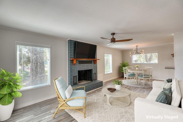 living room with light hardwood / wood-style floors, ceiling fan with notable chandelier, crown molding, and a fireplace