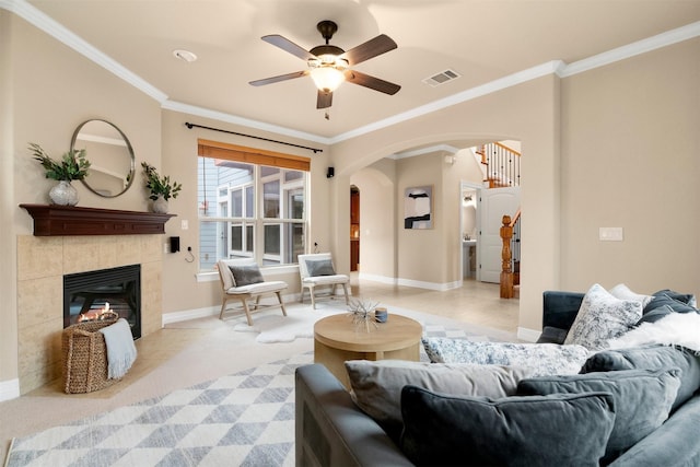 living room with a tiled fireplace, crown molding, and ceiling fan