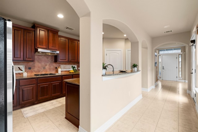 kitchen with dark stone countertops, backsplash, stainless steel appliances, and light tile patterned flooring