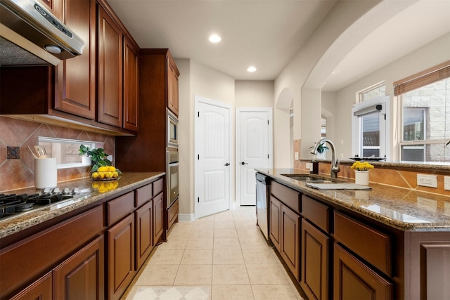 kitchen featuring appliances with stainless steel finishes, sink, dark stone countertops, decorative backsplash, and light tile patterned floors