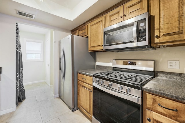 kitchen with light tile patterned flooring, dark stone counters, and appliances with stainless steel finishes