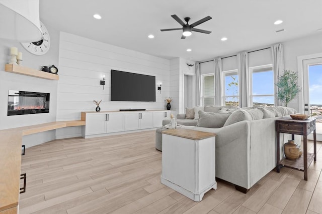 living area featuring light wood finished floors, a glass covered fireplace, a ceiling fan, and recessed lighting