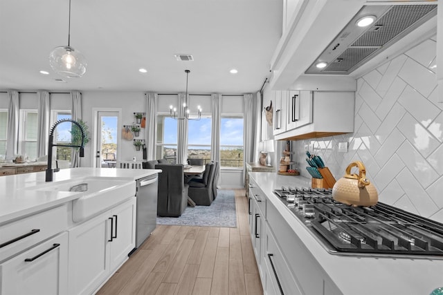 kitchen featuring white cabinets, custom range hood, appliances with stainless steel finishes, and pendant lighting