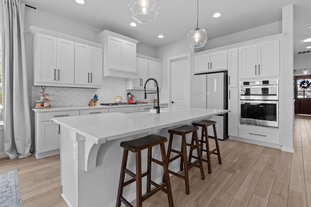 kitchen featuring appliances with stainless steel finishes, white cabinetry, decorative backsplash, a kitchen breakfast bar, and a kitchen island with sink