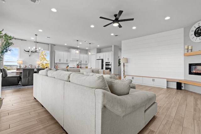 living room with a fireplace, ceiling fan with notable chandelier, sink, and light hardwood / wood-style flooring