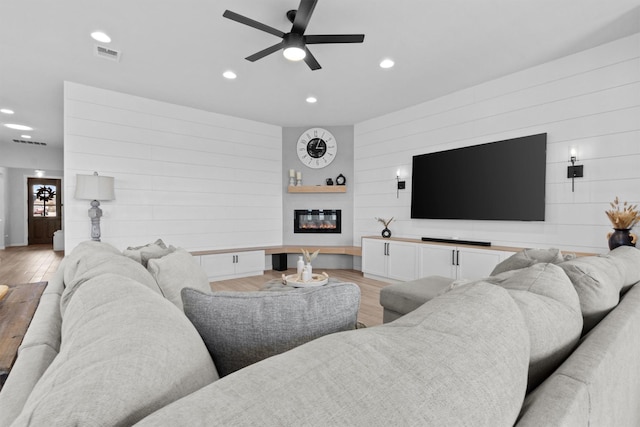 living room with light hardwood / wood-style floors, wooden walls, and ceiling fan