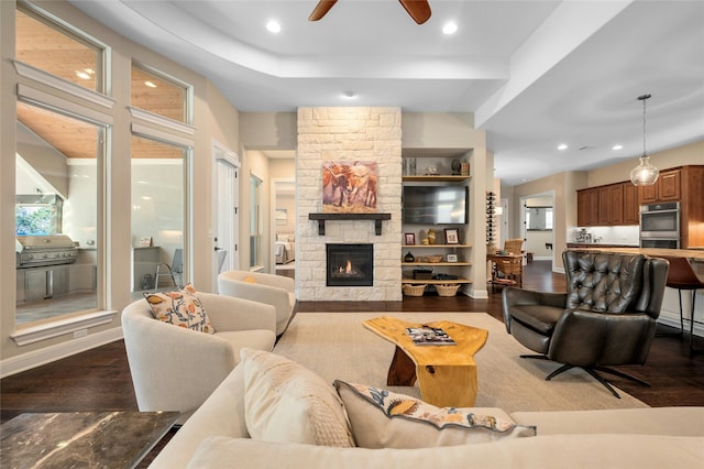 living room featuring built in features, ceiling fan, a stone fireplace, and dark hardwood / wood-style flooring