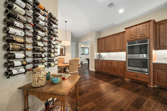 kitchen with double oven, dark hardwood / wood-style flooring, tasteful backsplash, hanging light fixtures, and light stone counters