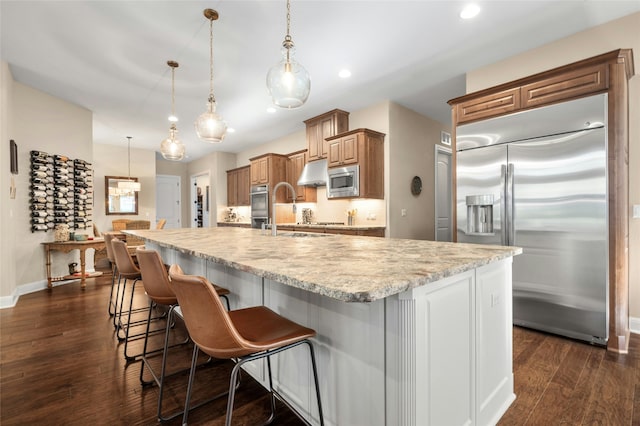 kitchen featuring a kitchen breakfast bar, pendant lighting, a large island, dark hardwood / wood-style floors, and built in appliances