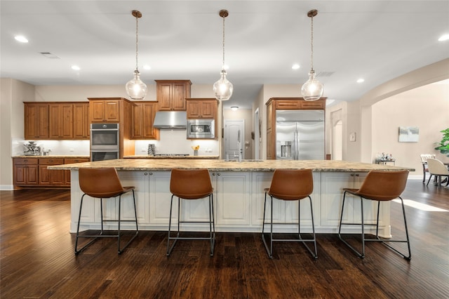 kitchen with a large island with sink, pendant lighting, and built in appliances