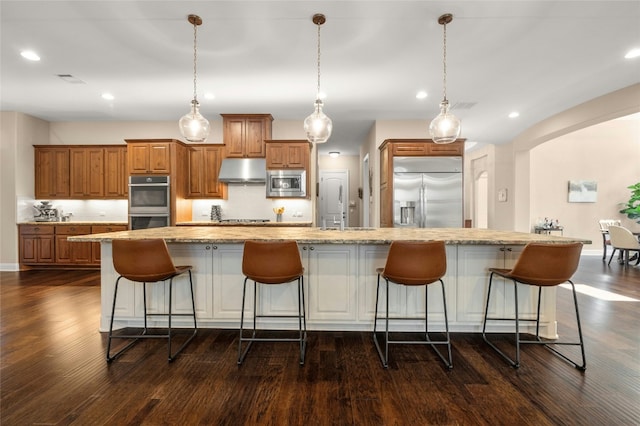 916 Morning Moon Cir, Austin, TX 78732 - kitchen with built in appliances, under cabinet range hood, brown cabinets, a breakfast bar area, and arched walkways