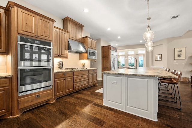 kitchen featuring pendant lighting, dark hardwood / wood-style flooring, tasteful backsplash, an island with sink, and built in appliances